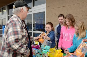 Girls sell Girl Scout Cookies to a man at a cookie booth sale.